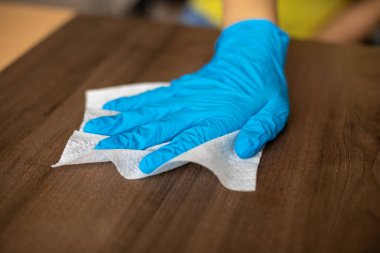 Mavi eldivenli bir kadın ev temizlik masası ahşap masa yüzeyini ıslak mendillerle temizliyor.