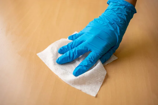 女性の手で青手袋消毒クリーニングホームオフィス木材テーブル表面でぬれたワイプ — ストック写真