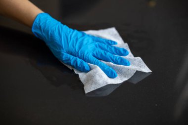 Mavi eldivenli bir kadın ofis masasını ıslak mendille temizliyor.