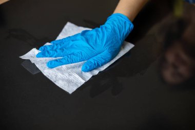 Mavi eldivenli bir kadın ofis masasını ıslak mendille temizliyor.