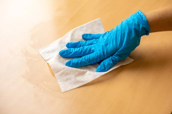 Woman\'s hand in blue gloves sanitizing cleaning home office wood table surface with wet wipes