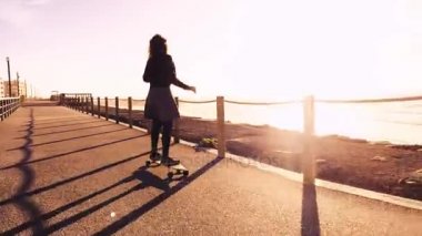 Kız günbatımında plaja yakın bir kaykay sürme.