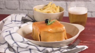 Geleneksel Portekiz aperatif yiyecek. Francesinha sandviç, ekmek, peynir, domuz eti, jambon, sosis, domates bira sos ve patates kızartması. Bira ve patates ile. Masada.