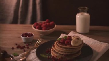 Ahududulu krepler, muz dilimleri, nar tohumları ve balı ahşap masa üzerinde..