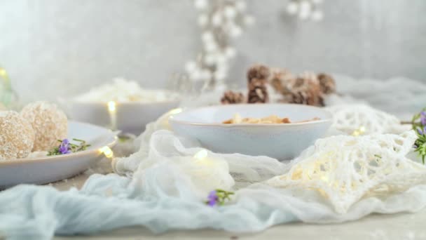 光と星で飾られたクリスマスシーズンのテーブルの上にココナッツローストアーモンドと自家製キャンディー — ストック動画