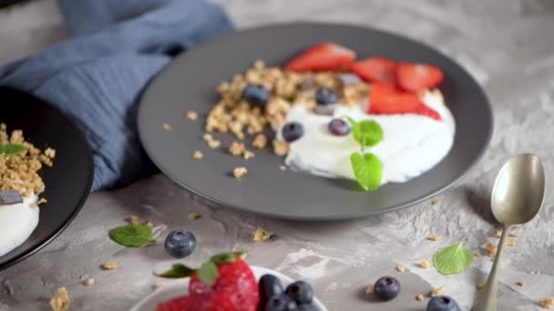 薄い灰色の背景にプレートにヨーグルトとグラノーラとブルーベリーとイチゴを熟す 健康的な食事 — ストック動画