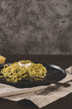 Karanlık mutfak tezgahında fesleğen soslu ve peynirli taze spagetti..