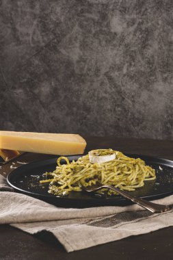 Karanlık mutfak tezgahında fesleğen soslu ve peynirli taze spagetti..