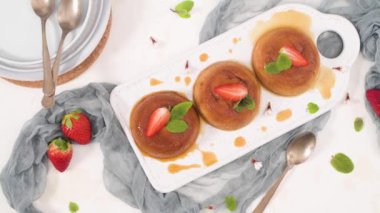 Beyaz seramik tepside ve mutfak tezgahında karamel kremalı puding..