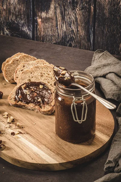 Vegan chocolate spread made of organic almond butter and organic cacao and honey, on dark rustic kitchen counter top.