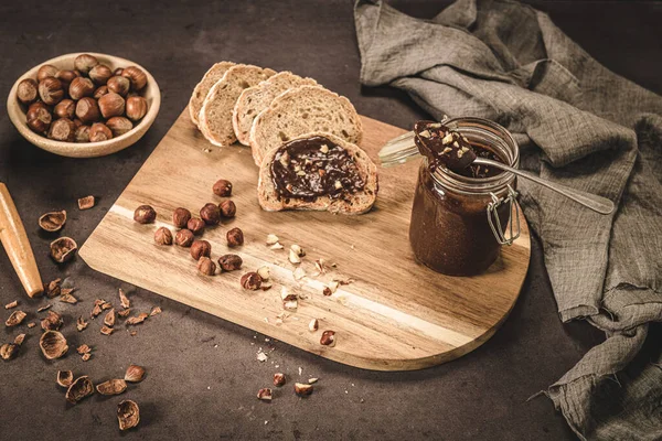 Vegan chocolate spread made of organic almond butter and organic cacao and honey, on dark rustic kitchen counter top.