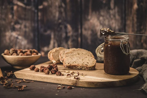 Vegan chocolate spread made of organic almond butter and organic cacao and honey, on dark rustic kitchen counter top.