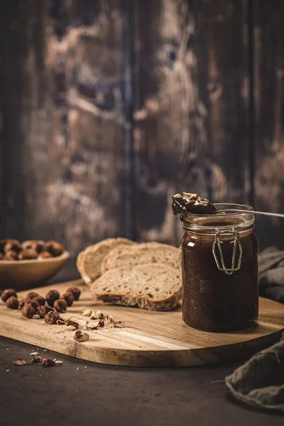 Vegan chocolate spread made of organic almond butter and organic cacao and honey, on dark rustic kitchen counter top.