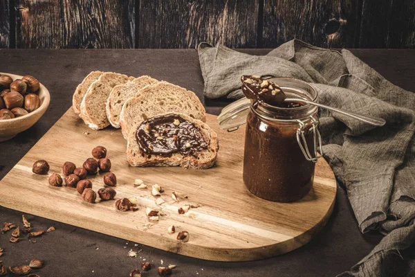 Vegan chocolate spread made of organic almond butter and organic cacao and honey, on dark rustic kitchen counter top.