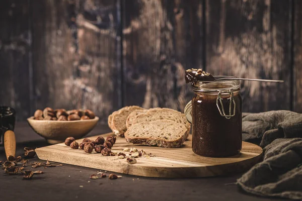 Vegan chocolate spread made of organic almond butter and organic cacao and honey, on dark rustic kitchen counter top.