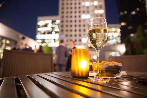 Glass of white wine and candle with evening view of city buildings