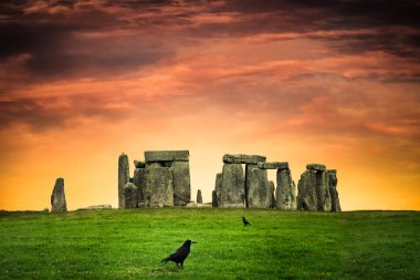 Siyah kargalarla renkli günbatımının altında tarihi Stonehenge