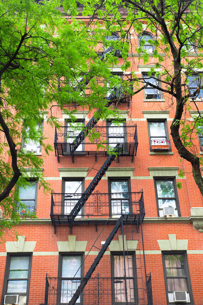 Typical New York City brick apartment building in spring surrounded by green trees.