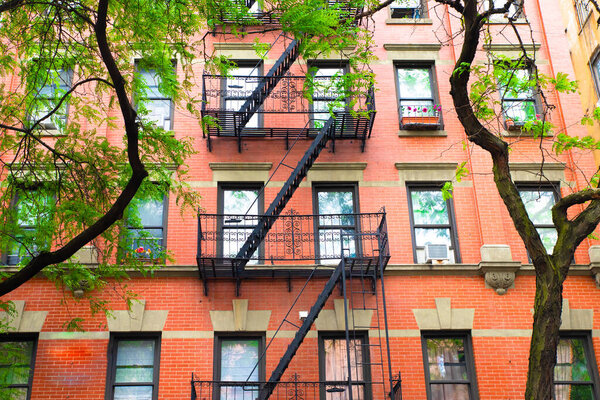 Typical New York City brick apartment building in spring surrounded by green trees.