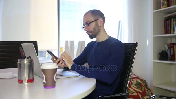 Der Mann mit Brille telefoniert und arbeitet mit Laptop — Stockvideo