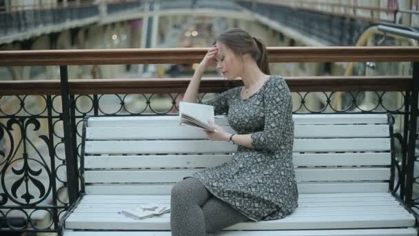 Jovencita leyendo un libro en el banco — Vídeo de stock