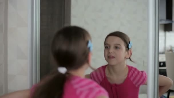 Маленькая девочка показывает лица перед зеркалом — стоковое видео