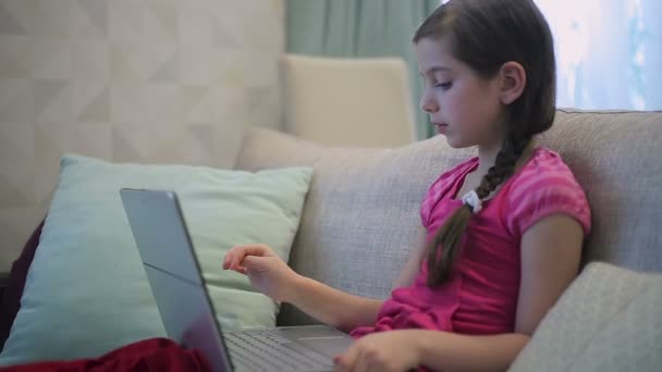 一个女孩坐在沙发上是教育在笔记本电脑上 — 图库视频影像