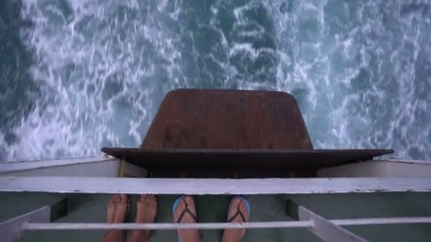 Pies de pareja en el barco y olas marinas detrás de un gran crucero — Vídeo de stock