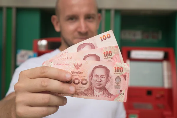 Closeup of 100 Thai Baht notes withdrawned from ATM over blurred man's face — Stock Photo, Image