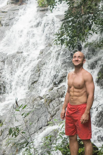 Щасливий красивий чоловік стоїть і дивиться вгору біля водоспаду — стокове фото