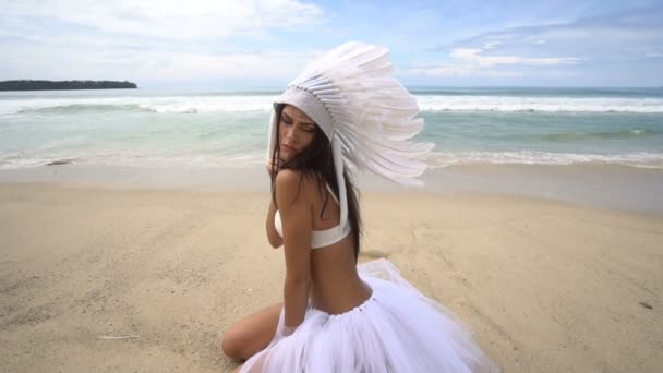Женщина в белой индийской шляпе с перьями на пляже — стоковое видео