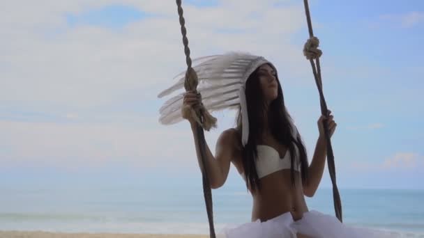 Mujer en sombrero de plumas indias blancas en la playa — Vídeo de stock