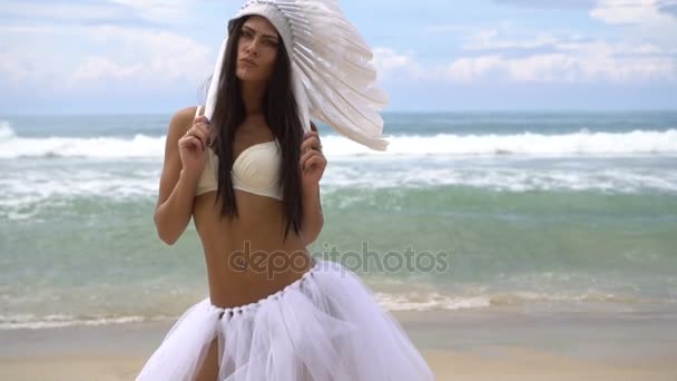 Mujer en sombrero de plumas indias blancas en la playa — Vídeo de stock