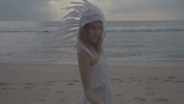 Vrouw met witte veren indiaanse hoed op het strand — Stockvideo