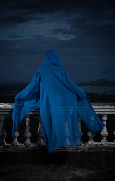 Vista posterior de la misteriosa mujer en bikini negro y capucha azul cubierta sentada en piedra vieja adornada barandilla tallada sobre el cielo nublado y paisaje urbano — Foto de Stock