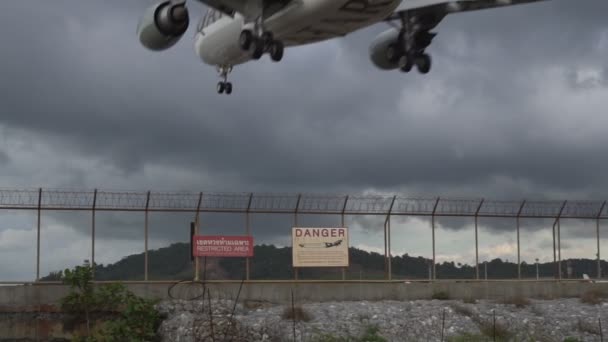 Flygplan landar på flygplatsen och varningsskylt på staketet över mulen himmel bakgrund — Stockvideo