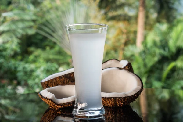 Cocos y agua de coco en la mesa de vidrio negro aislado sobre fondo de palmeras borrosas —  Fotos de Stock