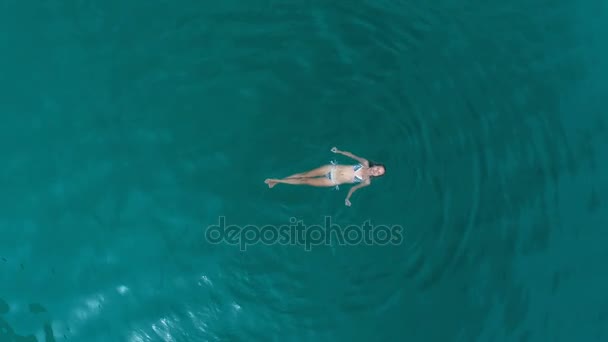 Вид с воздуха на женщину, отдыхающую в бирюзовой воде — стоковое видео