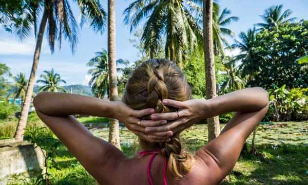 Женщина смотрит на красивый тропический вид с пальмами и маленьким прудом — стоковое фото