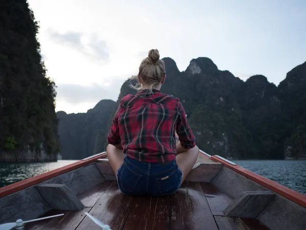 坐在木长的尾巴小船在热带石灰石峭壁和日落背景的妇女的后面看法 — 图库照片