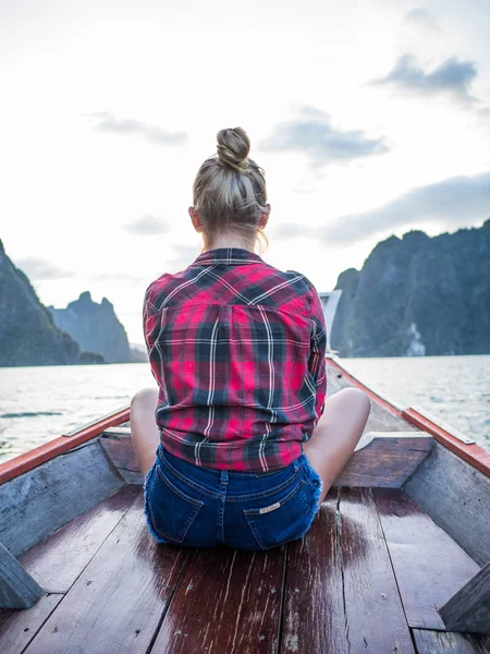 坐在木长的尾巴小船在热带石灰石峭壁和日落背景的妇女的后面看法 — 图库照片