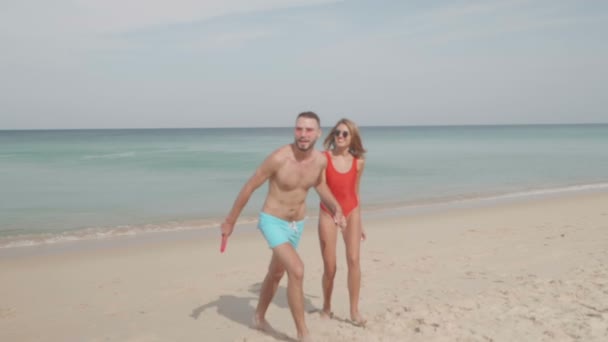 日当たりの良い夏の日 スローモーションのビデオ中に浜辺でフリスビー フライング ディスクで遊んで幸せなカップル — ストック動画