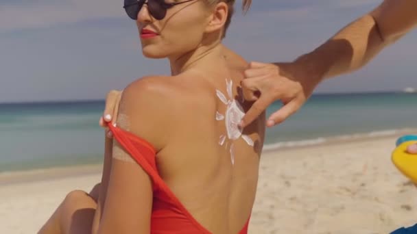 快乐的情侣在海滩上涂抹晒黑乳液 男人把防晒霜放在女人 视频慢动作 — 图库视频影像