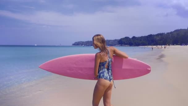 晴れた夏の日の中にピンクのサーフボードで海に歩いて若い幸せな女 彼女の熱帯のビーチの休日 スローモーションのビデオを楽しむ美少女 — ストック動画