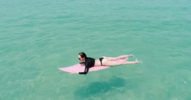 Güzel genç kadının mayo ve güneş gözlüğü şaşırtıcı berrak Denizi su - ağır çekimde video onun tatil keyfini pembe surfboard ile hava Üstten Görünüm