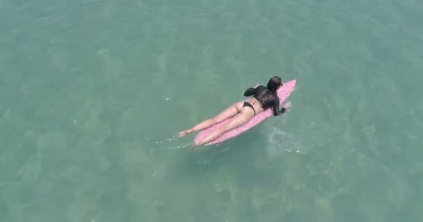 水着とサングラスに驚くほど澄んだ海の水で彼女の休日を楽しんでいるピンクのサーフボードの美しい若い女性の空中のトップ ビュー — ストック動画