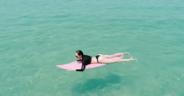 美丽的年轻女子在泳装和太阳镜与粉红色冲浪板的空中俯视图享受她的假期在惊人的清澈的海水 视频慢动作 — 图库视频影像