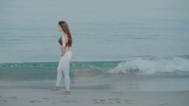美丽的女孩在沙滩上锻炼 美丽的年轻女孩在早晨在沙滩上锻炼 慢动作视频 — 图库视频影像