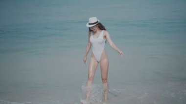 Güzel kız tropik sahilde / güzel kız mayo, şapka ve güneş gözlüğü yaz tatili sırasında deniz suyu - ağır çekimde video tropik sahilde rahatlatıcı