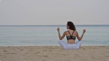 Arkadan görünüşü egzersiz / yoga sabahları kumsalda deniz ve gökyüzü arka plan üzerinde yaparken güzel genç kız
